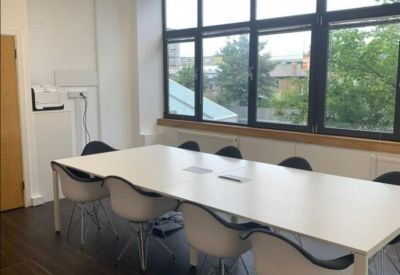 Bright boardroom featuring a long white table, white Eames-style chairs, and large windows.