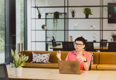 Professional in a pink shirt presenting from a laptop in a bright breakout area with plants.