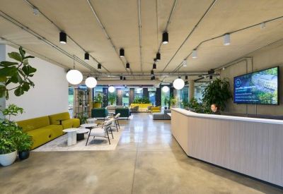 Expansive reception lobby with a white front desk, yellow sofas, and abundant greenery.