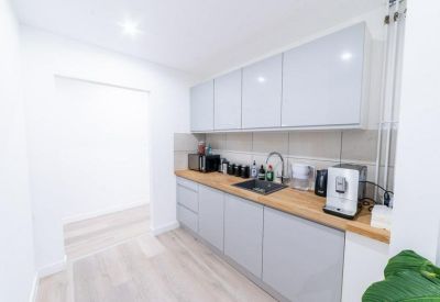 Modern communal kitchen with light grey cabinetry, wooden countertops, and coffee machine.
