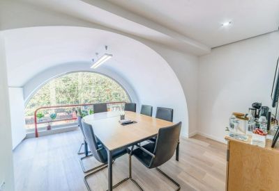 Bright meeting room with a large arched window overlooking trees and a wooden conference table.