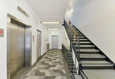 Bright white corridor featuring a lift entrance and a staircase with black railings.