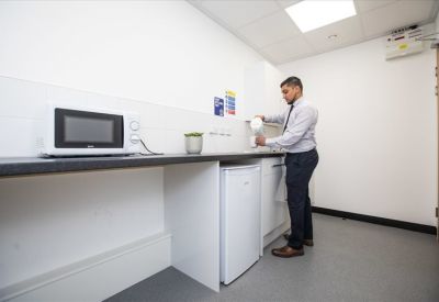 Modern kitchenette with a white fridge, microwave, and kettle being used by a professional.