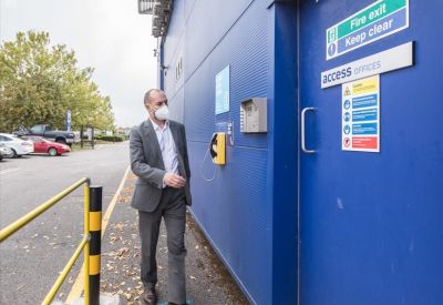 A man wearing a face mask uses an intercom system beside a blue exterior door.