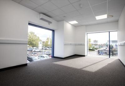 Spacious, empty office room with grey carpets and large windows overlooking a car park.