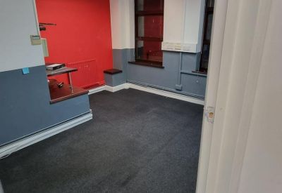 Small private office with a vibrant red accent wall and grey carpeting.