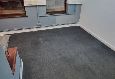 Empty office room with grey carpet and two large windows.
