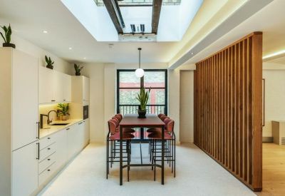 Clean white kitchen area with a high breakfast table, red chairs, and a skylight.