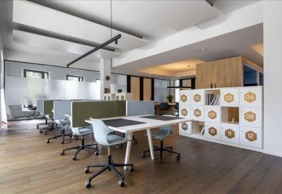 Open-plan coworking area with white desks, green dividers, and wooden flooring.