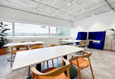 Modern coworking area with white tables, wooden chairs, and blue acoustic booths.
