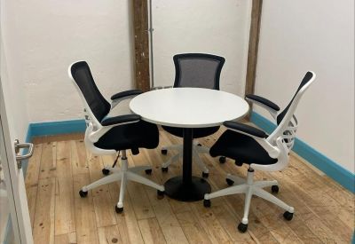 Four-person round meeting table in a bright room with exposed timber beams.
