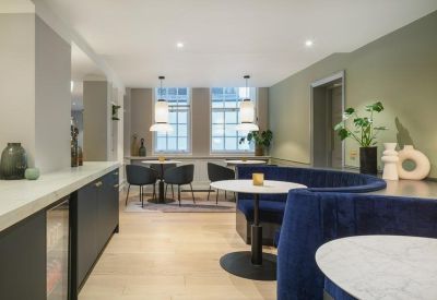 Modern communal break area with a curved blue velvet booth and sage green accent wall.
