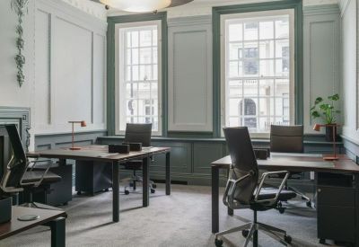 Light-filled private office with two dark wood desks and green wall panelling.