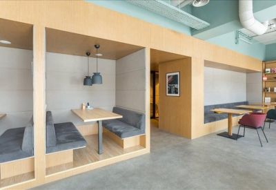 Modern communal breakout area with wooden booths, gray cushions, and blue pendant lights.