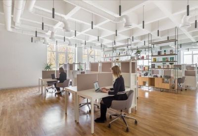 Spacious open-plan workspace with wooden floors, white desks, and industrial ceiling details.