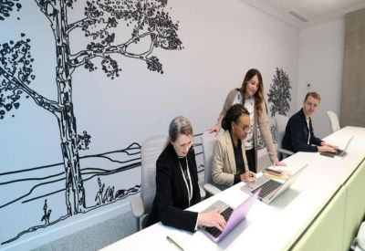 People working at a long white desk with a large tree mural on the wall.