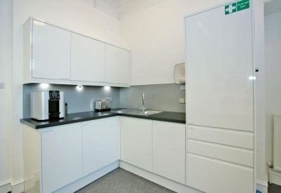 Modern white kitchenette with integrated appliances and under-cabinet lighting.