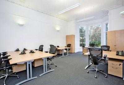 Spacious open-plan office with multiple desks, black mesh chairs, and large windows.