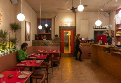 Reception and cafe counter with red tabletops, wooden stools, and warm orb lighting.