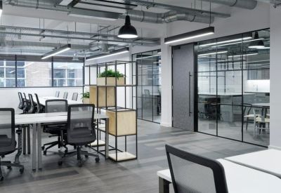 Open-plan office with white desks, ergonomic mesh chairs, and exposed ceiling ductwork.