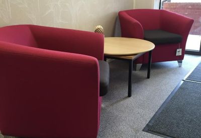 Communal waiting area featuring two bright pink tub chairs and a round wooden coffee table.