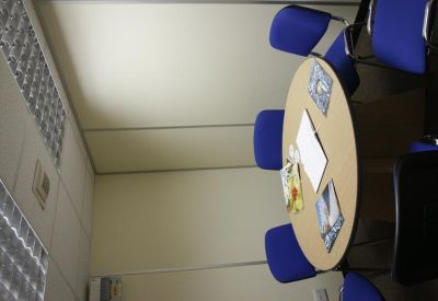 Small meeting room with a round wooden table surrounded by blue office chairs.