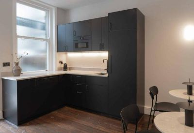 Modern black kitchen with white countertops and a small dining area.