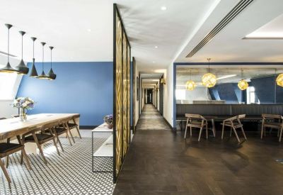 Communal breakout area featuring a long wooden table, blue accent wall, and designer pendant lights.