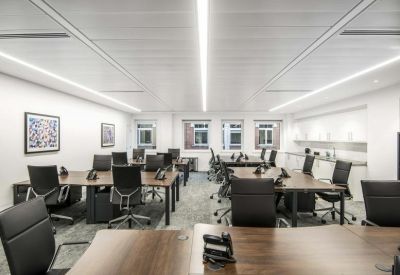 Bright open-plan office with wood-topped desks and modern black ergonomic chairs.