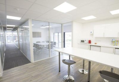 Bright communal kitchen and breakout area with high stools, white cabinetry, and wood-effect flooring.
