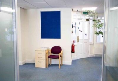 Reception area featuring a blue notice board, a purple armchair, and wooden pedestal unit.