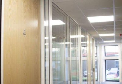 Bright hallway corridor with glass-walled office suites and numbered wooden doors.