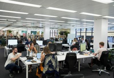 Open-plan office space with rows of white desks and people working at monitors.