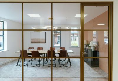 Modern meeting room viewed through an industrial glass partition with leather chairs.