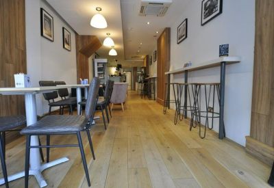 Narrow communal café area with wooden floors, pendant lighting, and high tables.