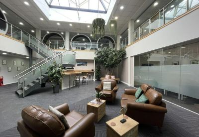 Spacious sunlit atrium at 2010 The Crescent, Solihull Parkway with leather seating and a glass-walled staircase.