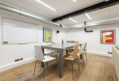 Bright meeting room with a central grey table, wooden chairs, and colorful wall art.