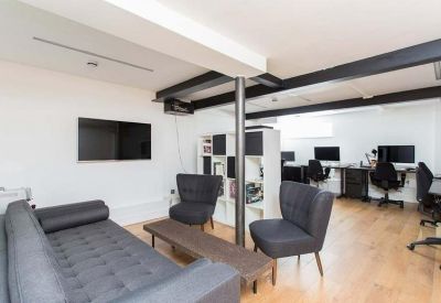 Modern coworking area featuring a large grey sofa, dark armchairs, and workstations in the background.