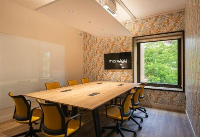 Professional meeting room with a large wooden table, yellow mesh chairs, and floral wallpaper.