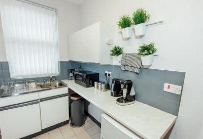 Modern communal kitchen with white cabinetry, grey backsplash, and potted plants.