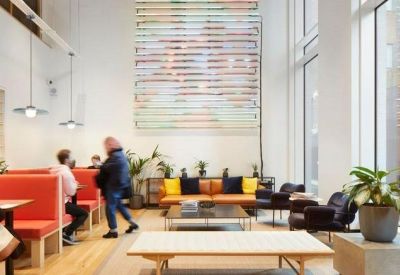 High-ceiling reception lobby with bright orange booth seating and a large abstract wall hanging.