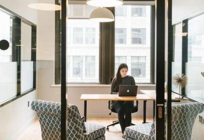 Private glass-walled office suite with a person working at a desk and patterned armchairs.