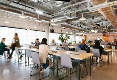 Bright open-plan coworking area with long wooden tables and industrial ceiling details.