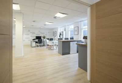 Workspace entrance view showing a break area with grey cabinetry and light wood flooring.