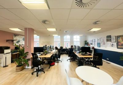 Bright open-plan office featuring pink structural columns and shared wooden desks.