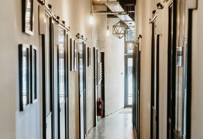 Narrow industrial-style corridor with glass-partitioned office doors and warm pendant lighting.