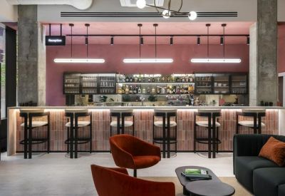 Reception bar area with pink walls, pendant lighting, and rows of stylish bar stools.