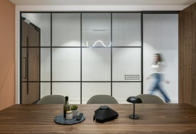 Meeting room table foregrounding a black framed glass partition with a person walking past.