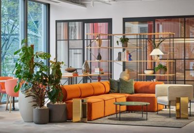 Lounge area with a vibrant orange modular sofa, potted plants, and a black-framed glass partition.