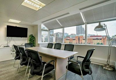 Meeting room with a long wooden table, black ergonomic chairs, and city views.